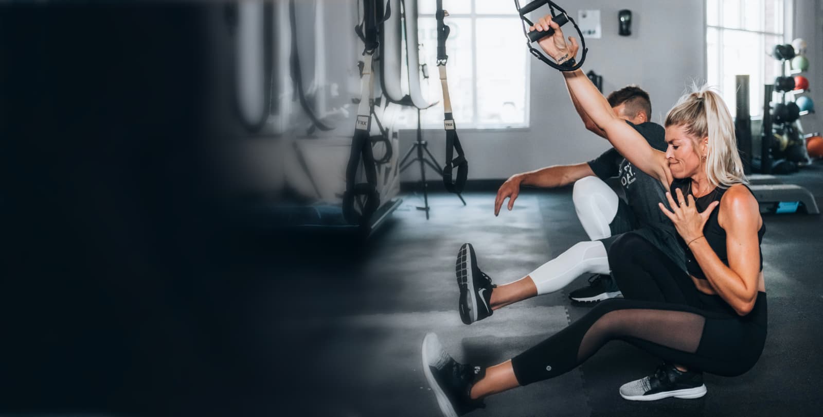 Frau führt TRX Suspension Training mit Personal Trainer im modernen Fitnessstudio durch