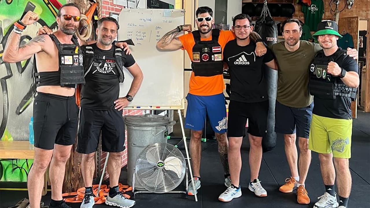 Sechs Männer mit Gewichtswesten posieren nach dem Training im CrossFit-Studio